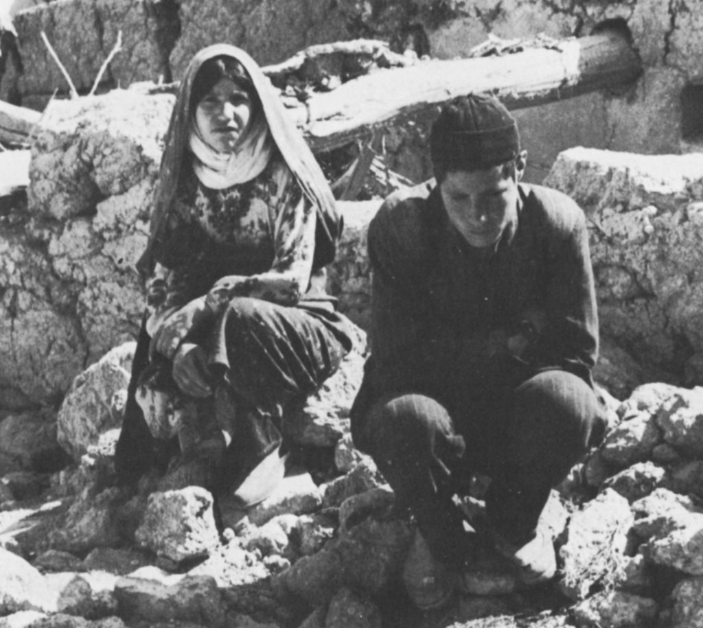 A woman and a man squat in rubble