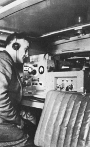 A man in headphones in front of a panel with dials and gauges