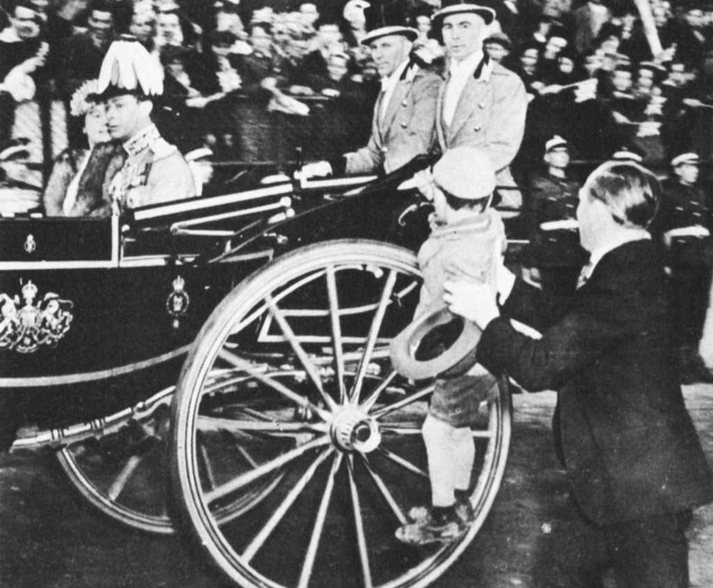 A small boy is lifted up to see the King and Queen go by in a carriage