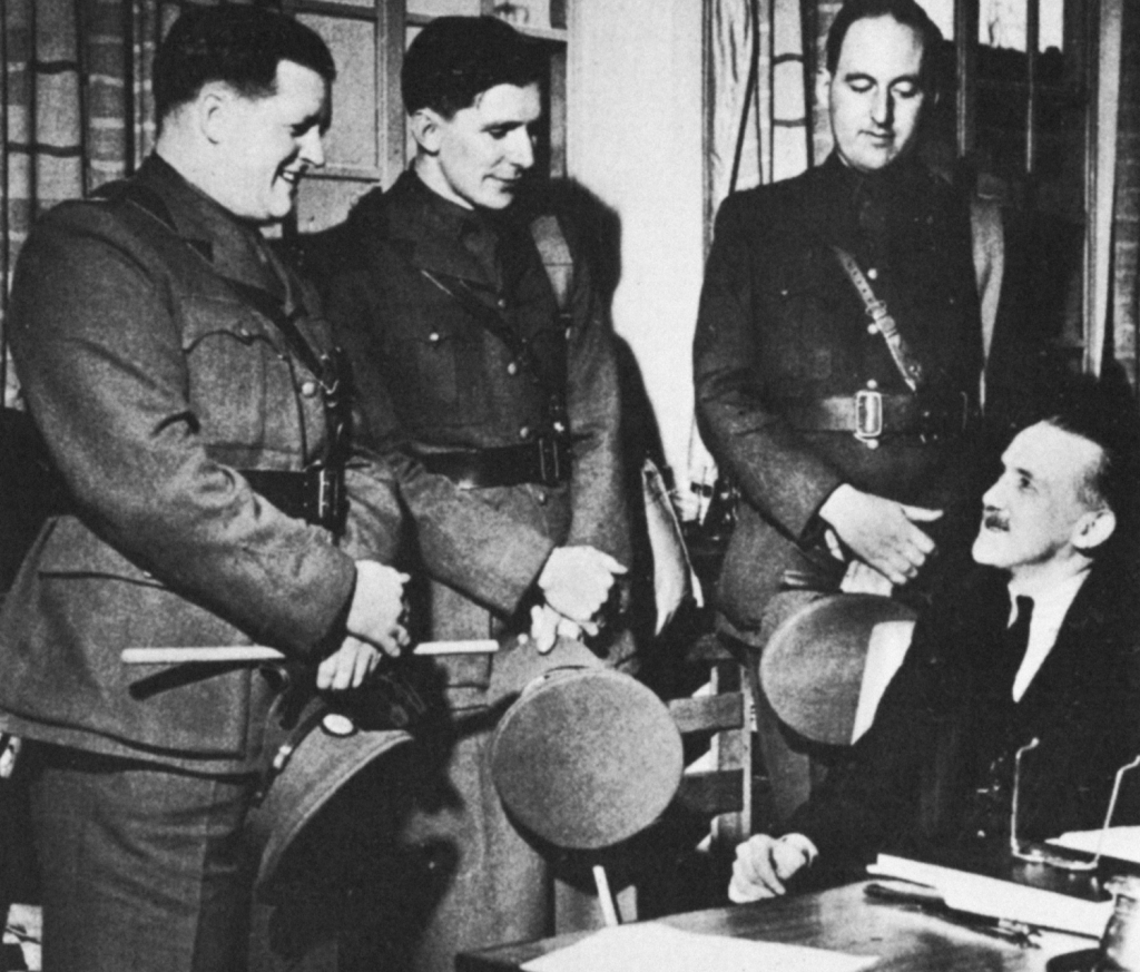 Three men in uniform talk to a man in a suit