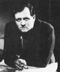 Dimbleby leans over a desk, holding a cigarette